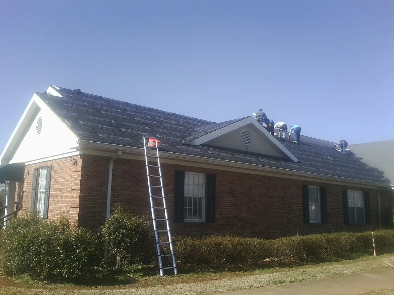 Crew tearing shingles off a brick ranch roof with a ladder set — Emergency Roof Repair work by our crew in Rockaway