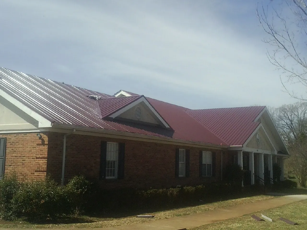 Red metal roof with gabled entries on a long brick building, from a Hail Damage Roof Repair job in Rockaway
