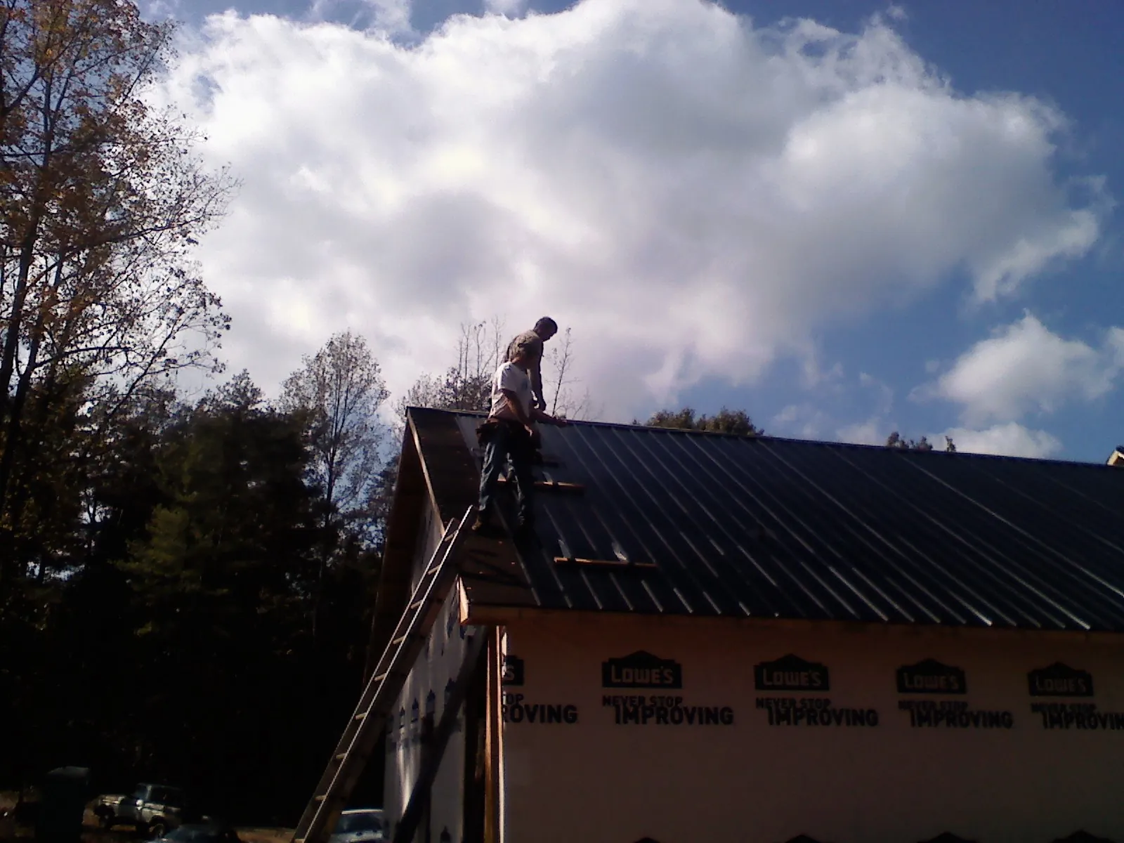 Roofer fastening dark metal panels high against a cloudy sky, from a Roof Inspection job in Rockaway