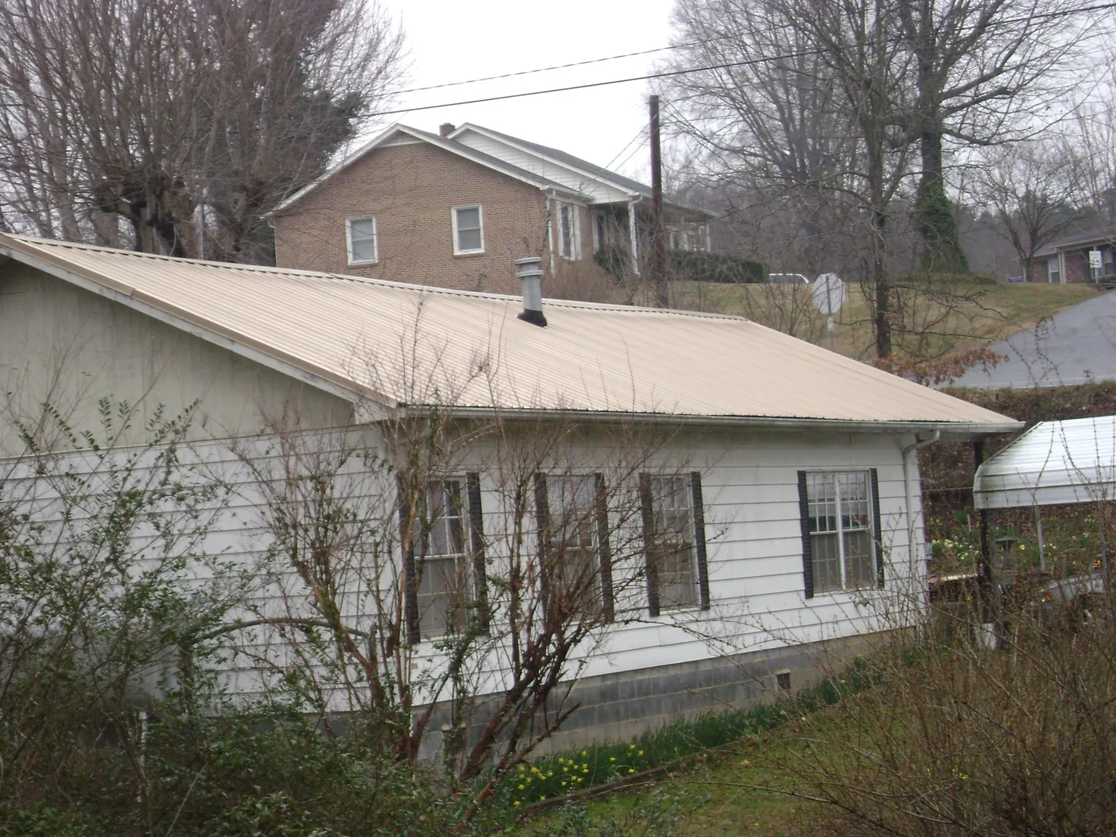 Tan metal roof on a white sided house set into a hillside — Commercial Roofing by Roofing Brothers in Rockaway